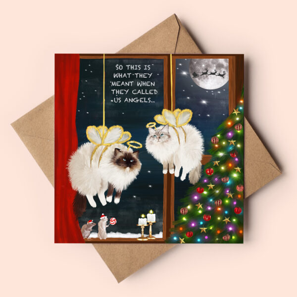 Cute cat themed christmas card featuring two fluffy ragdoll cats dressed with angel wings. They seem to be suspended in the festive window and look a bit put out. Text reads: Should have known something was up, when they called us angels! Behind them the night sky is visible though the window and the silhouette of Santa can be seen againts a full moon. Next to them is a christmas tree and little mouse holding candy cane.