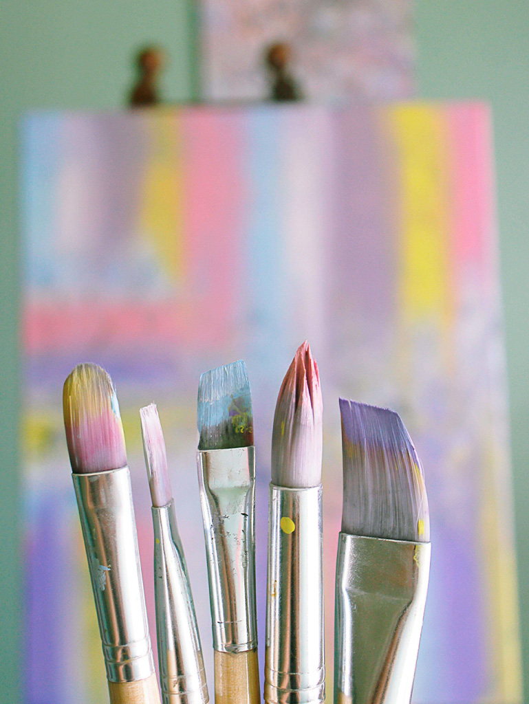 Beautiful pastel paint stained brushes with a canvas in the background, inspiring artists to create on bad days too.